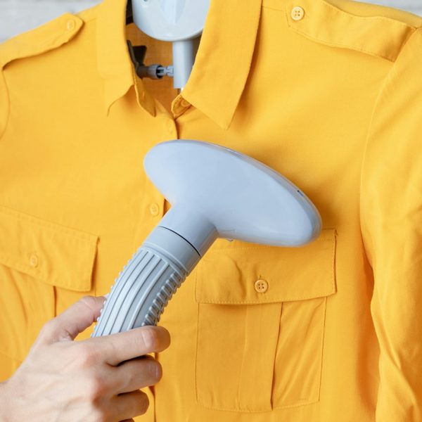 female hand using vertical steamer steaming clothes